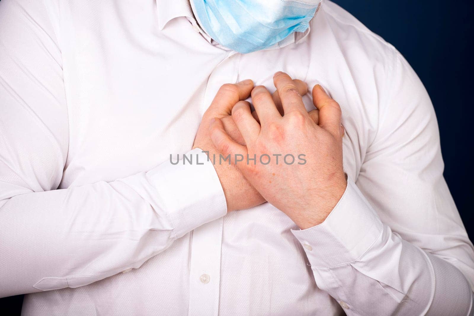 Man wearing medical face mask with chest pain - heart attack, shortness of breath during work in office.