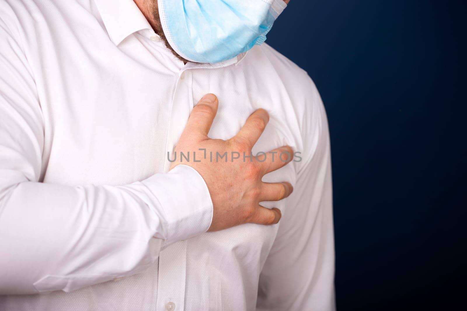 Man wearing medical face mask with chest pain - heart attack, shortness of breath during work in office.