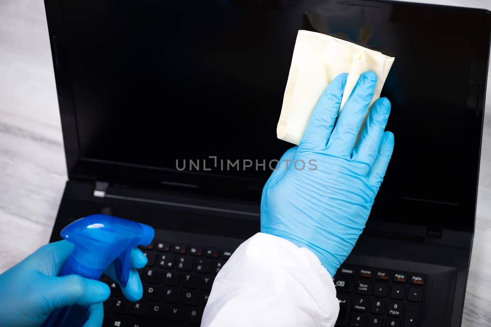 Office sanitizing wiping laptop with disinfectant. Coronavirus COVID-19 sanitize cleaning, disinfection of work desk.