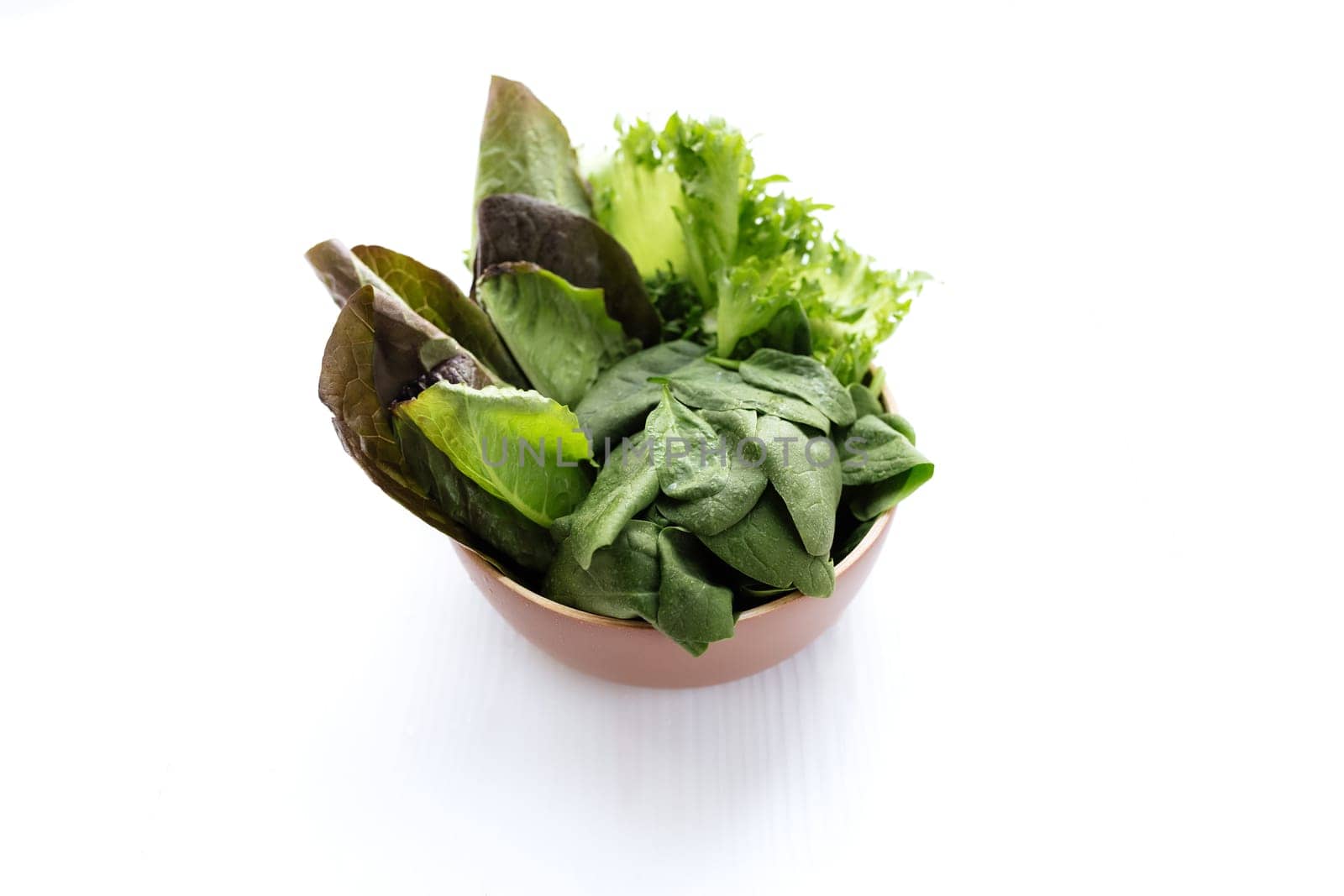 Flat lay with bowl of fresh green salad leaves of spinach and lettuce, romaine and basil on white background. Healthy vegetarian eating concept. High quality photo