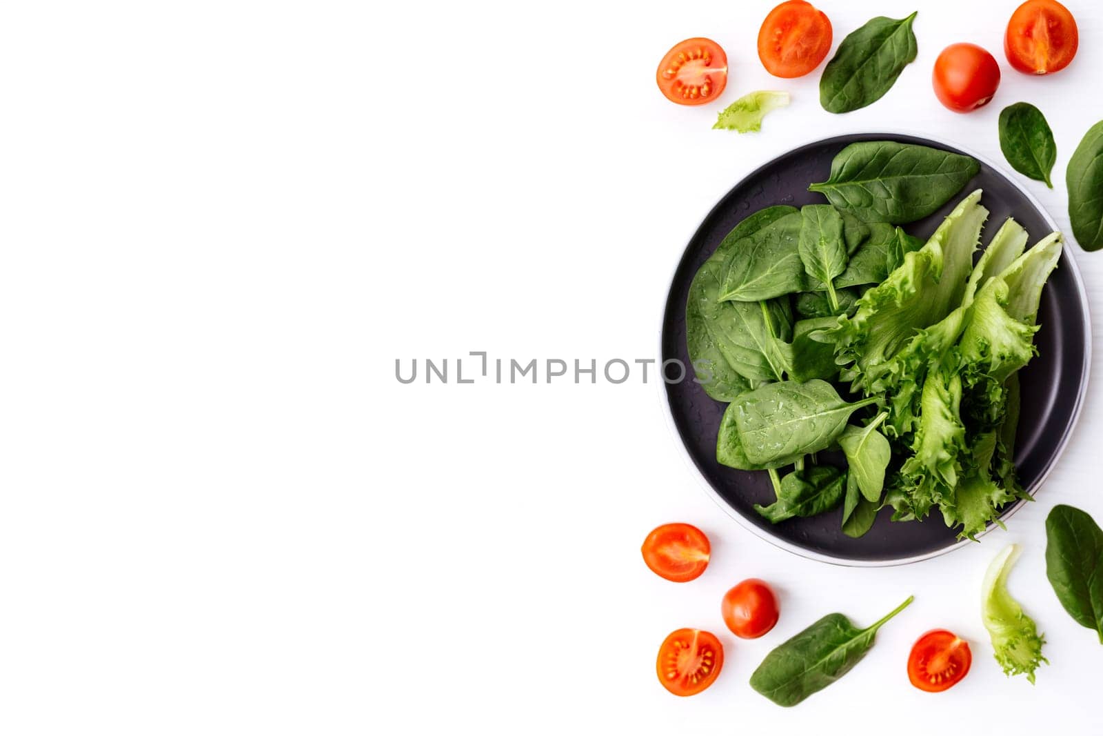 Flat lay with bowl of fresh green salad leaves, lettuce, spinach and red cherry tomatoes cups and halves on a white background. Healthy vegetarian eating concept. High quality photo