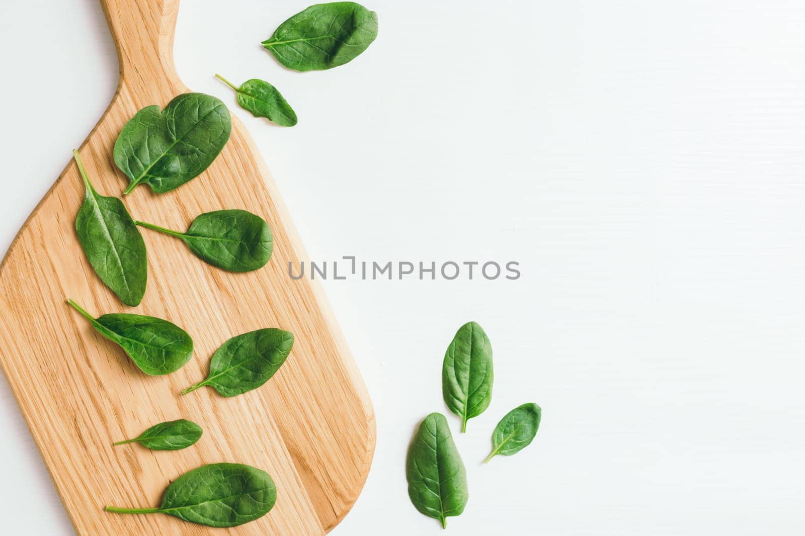 Wooden cutting board with fresh green salad leaves of spinach on white background. Healthy vegetarian eating concept. High quality photo