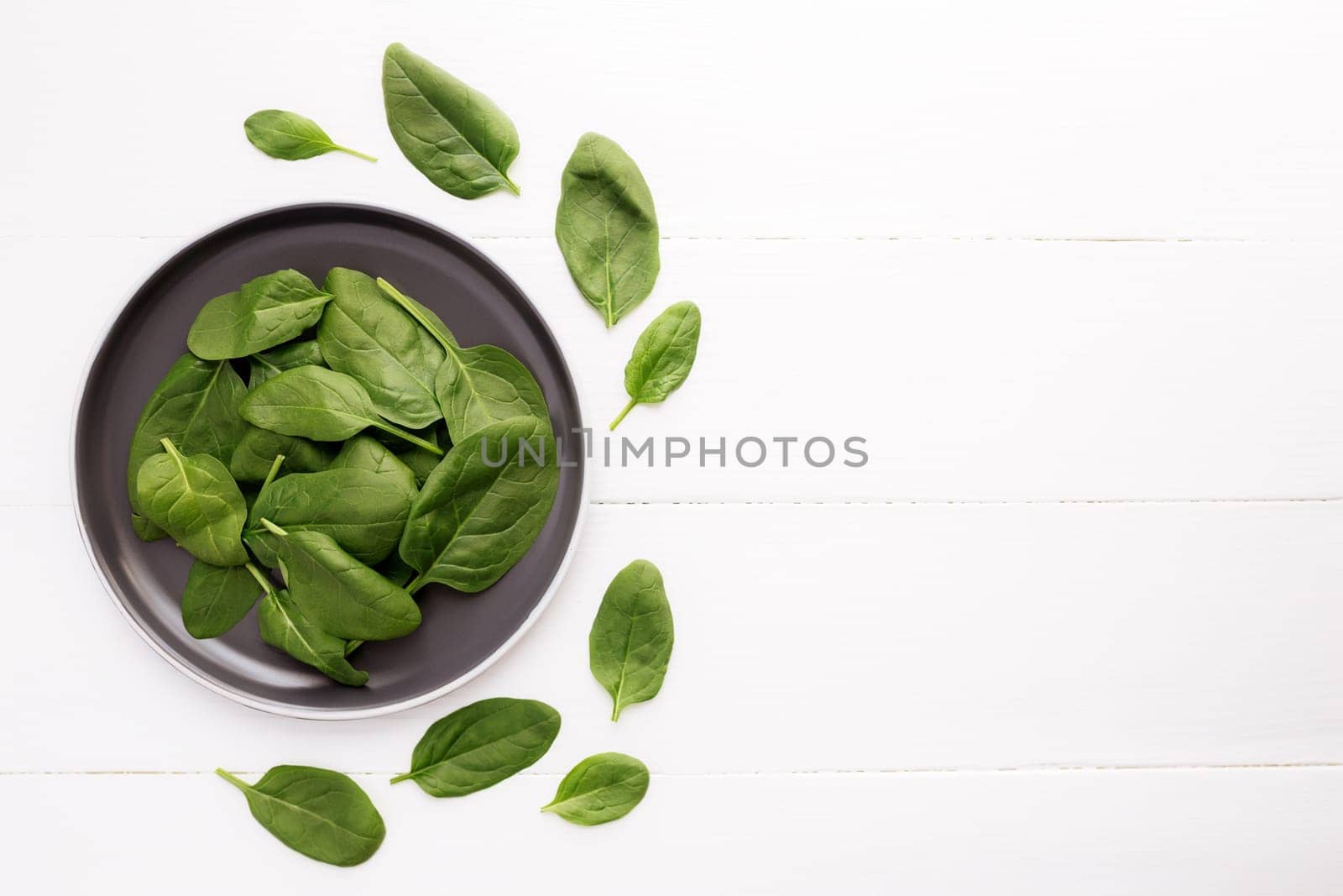 Bowl with fresh green salad leaves of spinach on a white background. Healthy vegetarian eating concept. High quality photo
