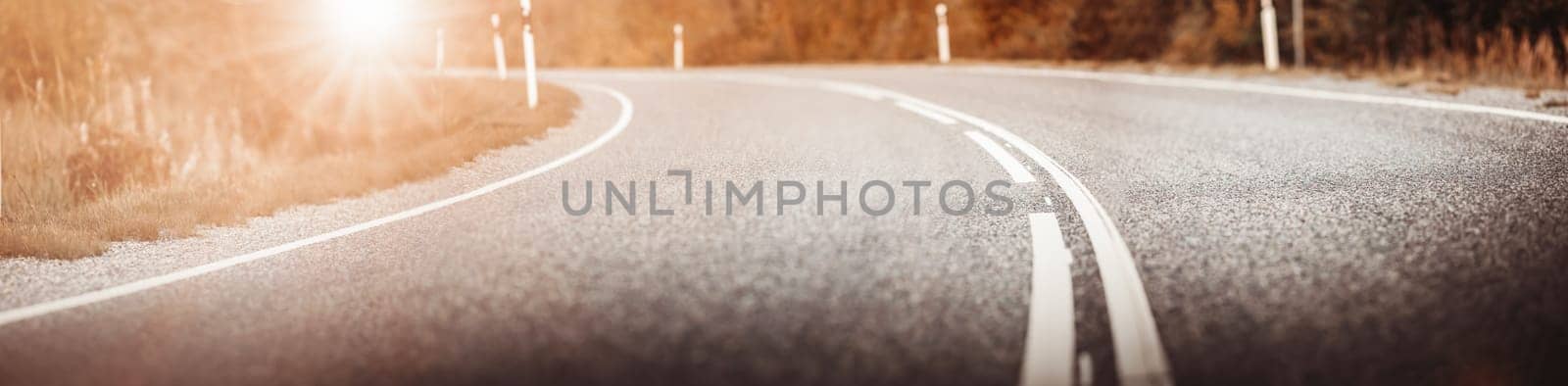 Asphalt road panorama in countryside on sunset in summer. Route with white dividing lines in beautiful nature landscape.
