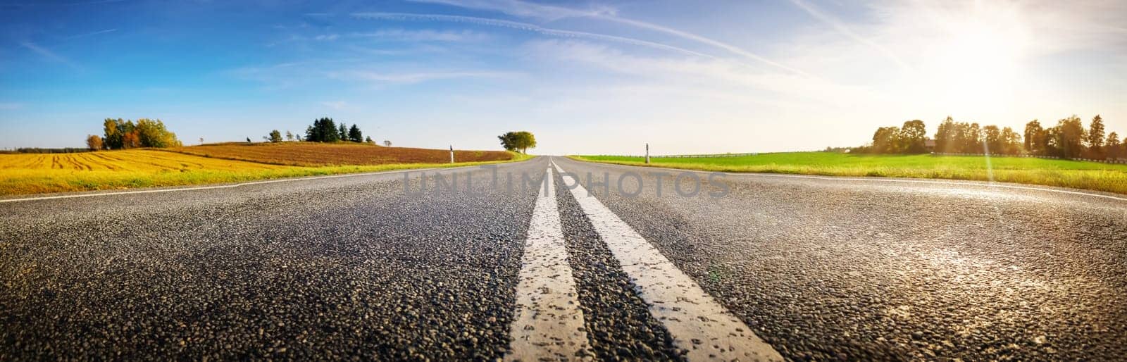 Wide asphalt road panorama in countryside on summer day. Route with white dividing lines in beautiful nature landscape.