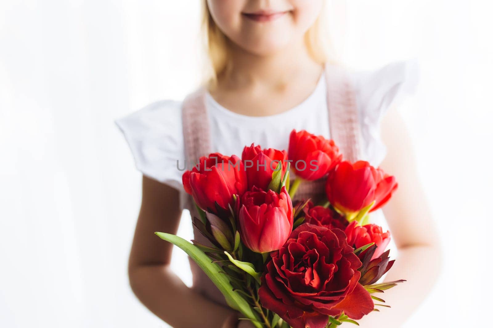 Small smiling girl holding bouquet of red tulip flowers. Concept for greeting card for Easter, Mother's day, International women's day, Saint Valentine's day. High quality photo