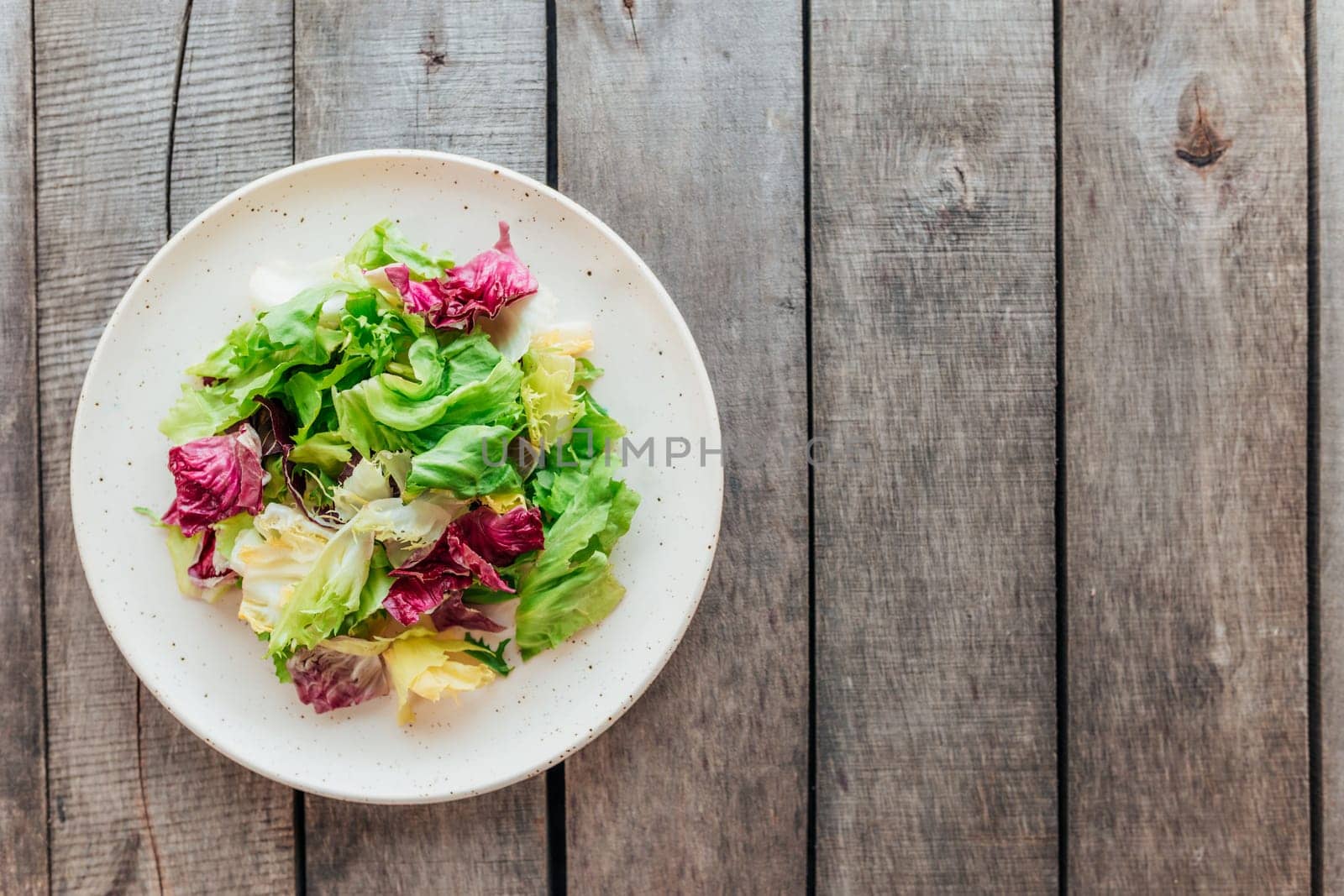 Healthy eating concept flat lay. Plate with mix of fresh green salad leaves, lettuce radicchio, basil on wooden background. Healthy eating concept. Vegetarian concept. Vegan food. Gardening concept.