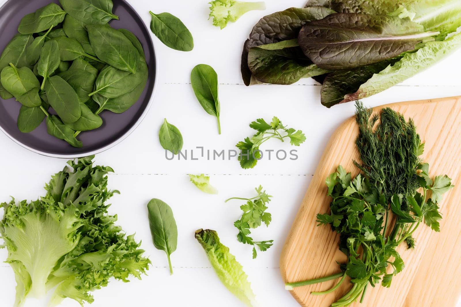 Flat lay with cutting board and bowl of fresh green salad leaves of spinach and lettuce, romaine and parsley, basil on white background. Healthy vegetarian eating concept. High quality photo