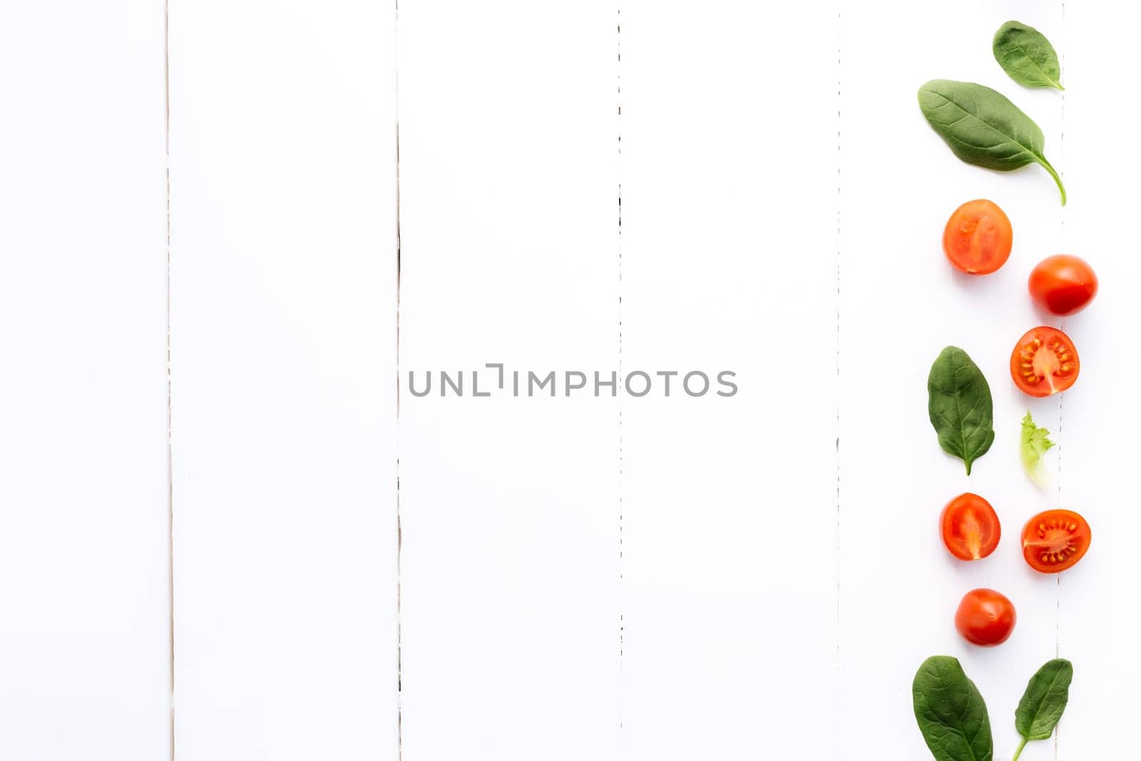 Flat lay with red cherry tomatoes and green spinach leaves on a white wooden background. Healthy eating concept. High quality photo