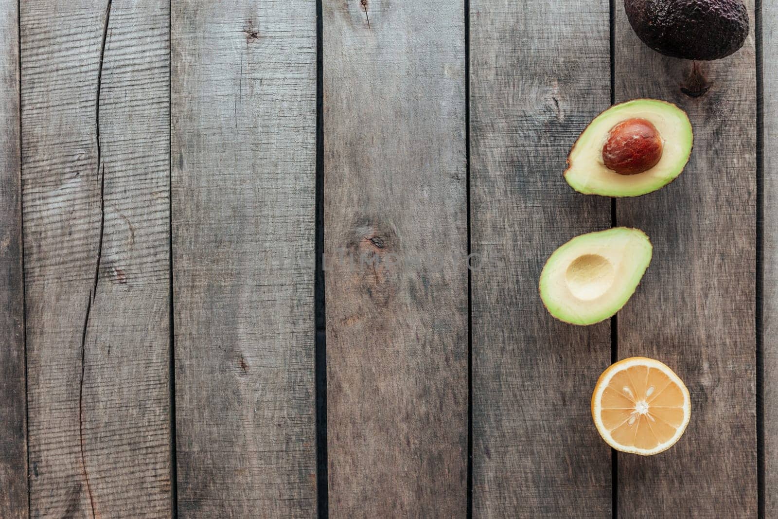 Healthy eating concept flat lay. Mediterranean diet, wooden background with avocado halves, whole avocado, avocado kernel, lemon half. Vegetarian food. Healthy food concept. Organic food