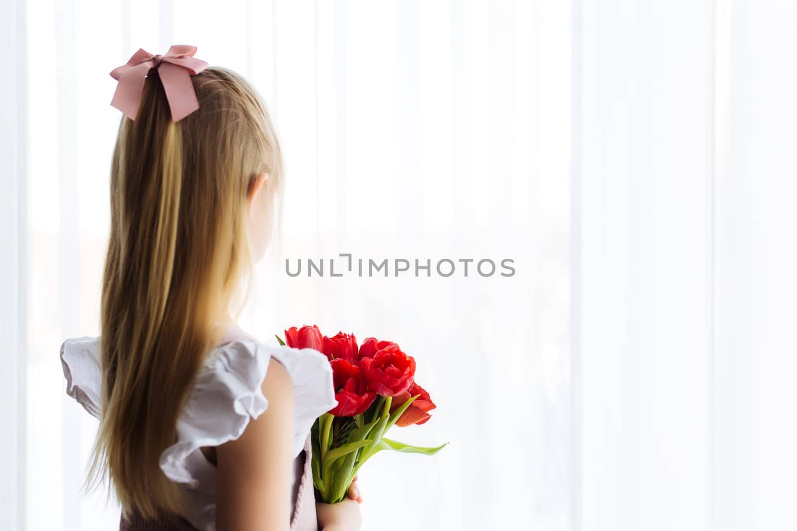 Small girl holding bouquet of red tulip flowers. Concept for greeting card for Easter, Mother's day, International women's day, Saint Valentine's day. High quality photo