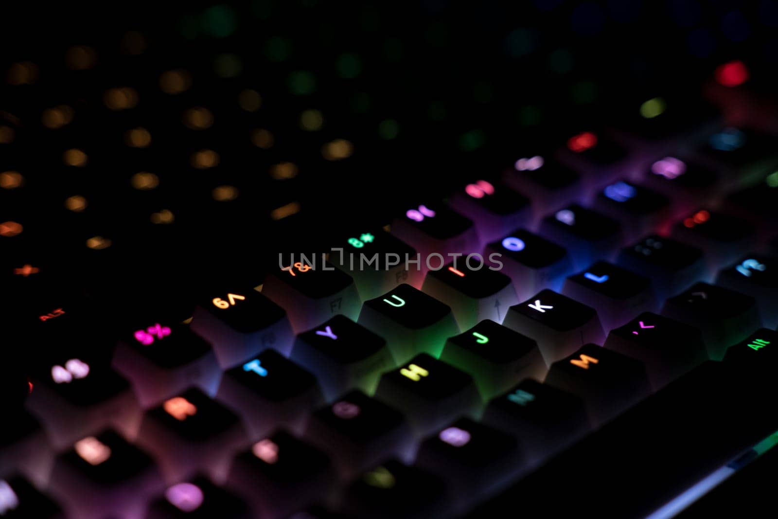 top view detail closeup of two illuminated mechanical gaming RGB keyboard with keycaps lighting up in different colors in the dark