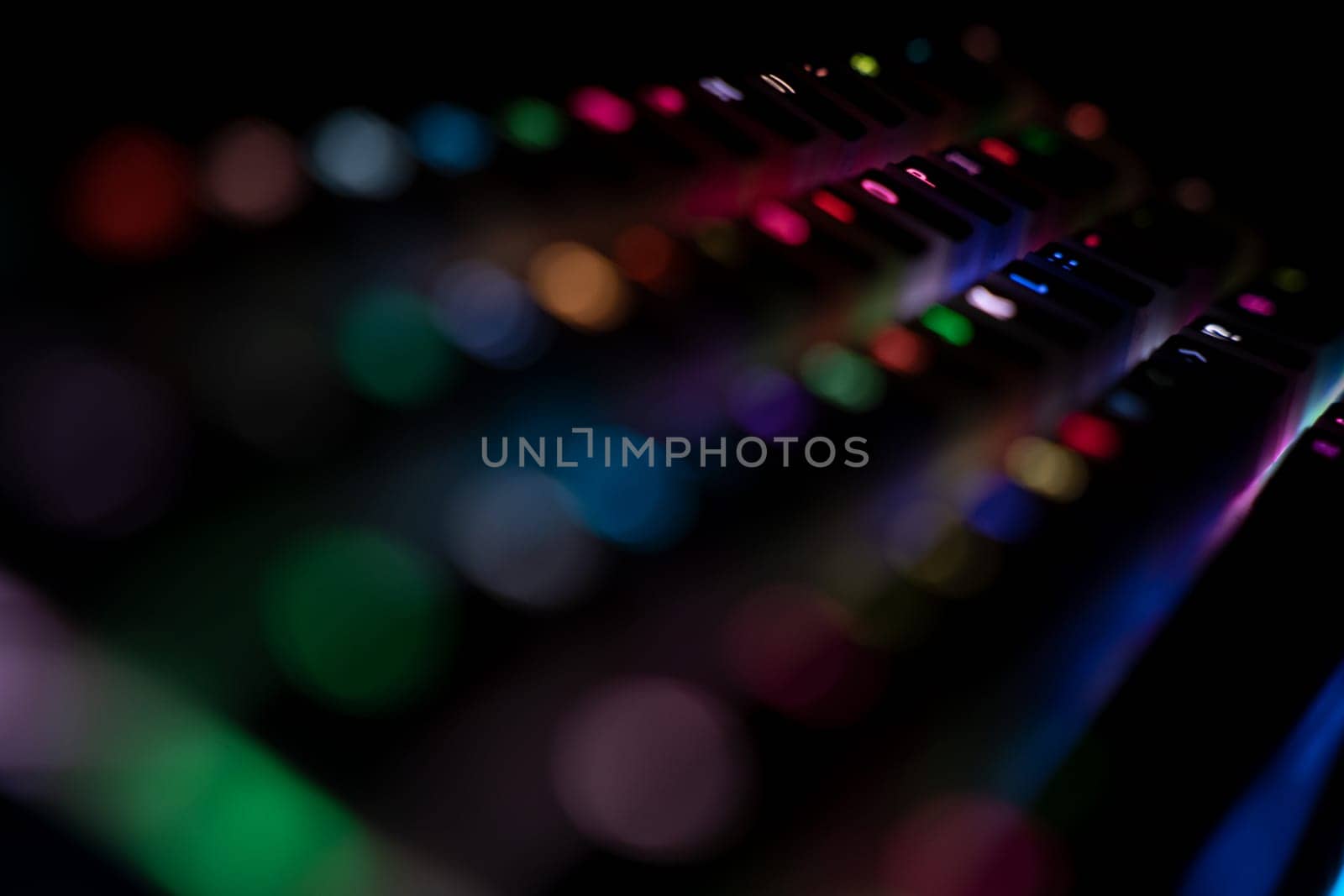 perspective side view detail closeup with shallow depth of field of illuminated mechanical gaming RGB keyboard with keycaps lighting up in different colors in the dark
