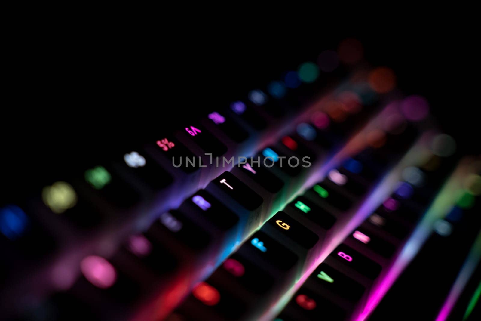 perspective side view detail closeup with shallow depth of field of illuminated mechanical gaming RGB keyboard with keycaps lighting up in different colors in the dark