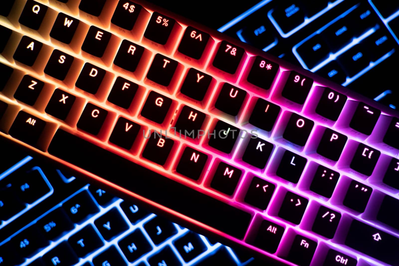 top view detail closeup of two illuminated mechanical gaming RGB keyboard on black desk on top of each other with keycaps lighting up in different colors in the dark