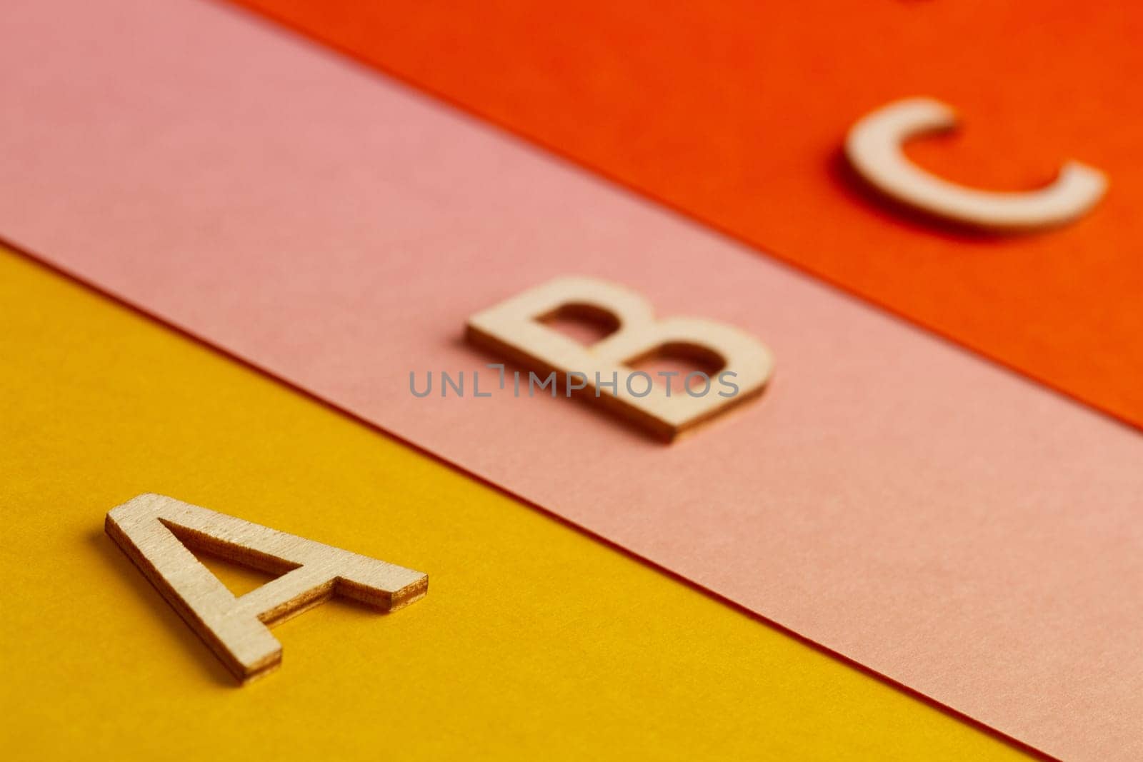 side view perspective closeup of A B and C letters of the alphabet cut in wood on colored paper background