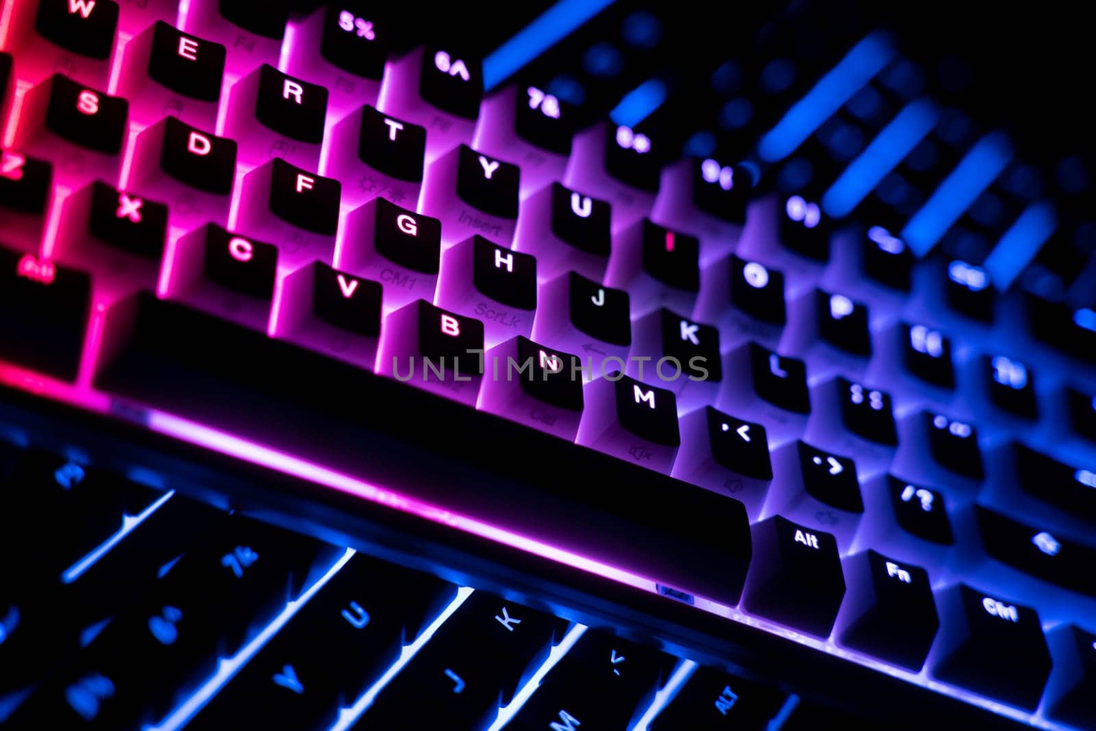 side view detail closeup of two illuminated mechanical gaming RGB keyboard on black desk on top of each other with keycaps lighting up in different colors in the dark