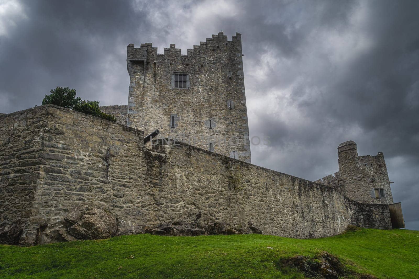 Cannon sticking out from fortification wall of 15th century Ross Castle with dramatic storm clouds in background, Ring of Kerry, Killarney, Ireland