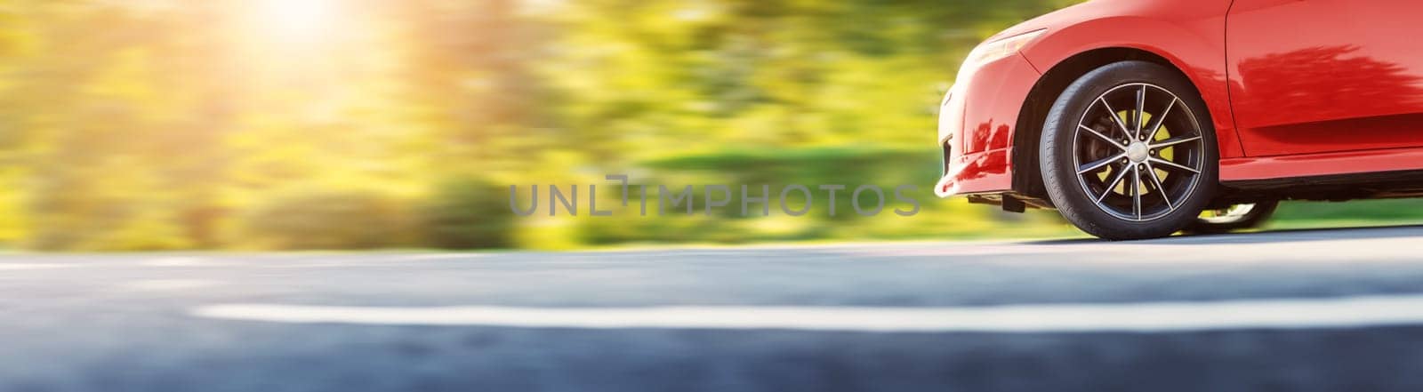Red car on asphalt road on summer sunlight. Beautiful panoramic view of the auto on the highway in the park. Concept of the family vacations.