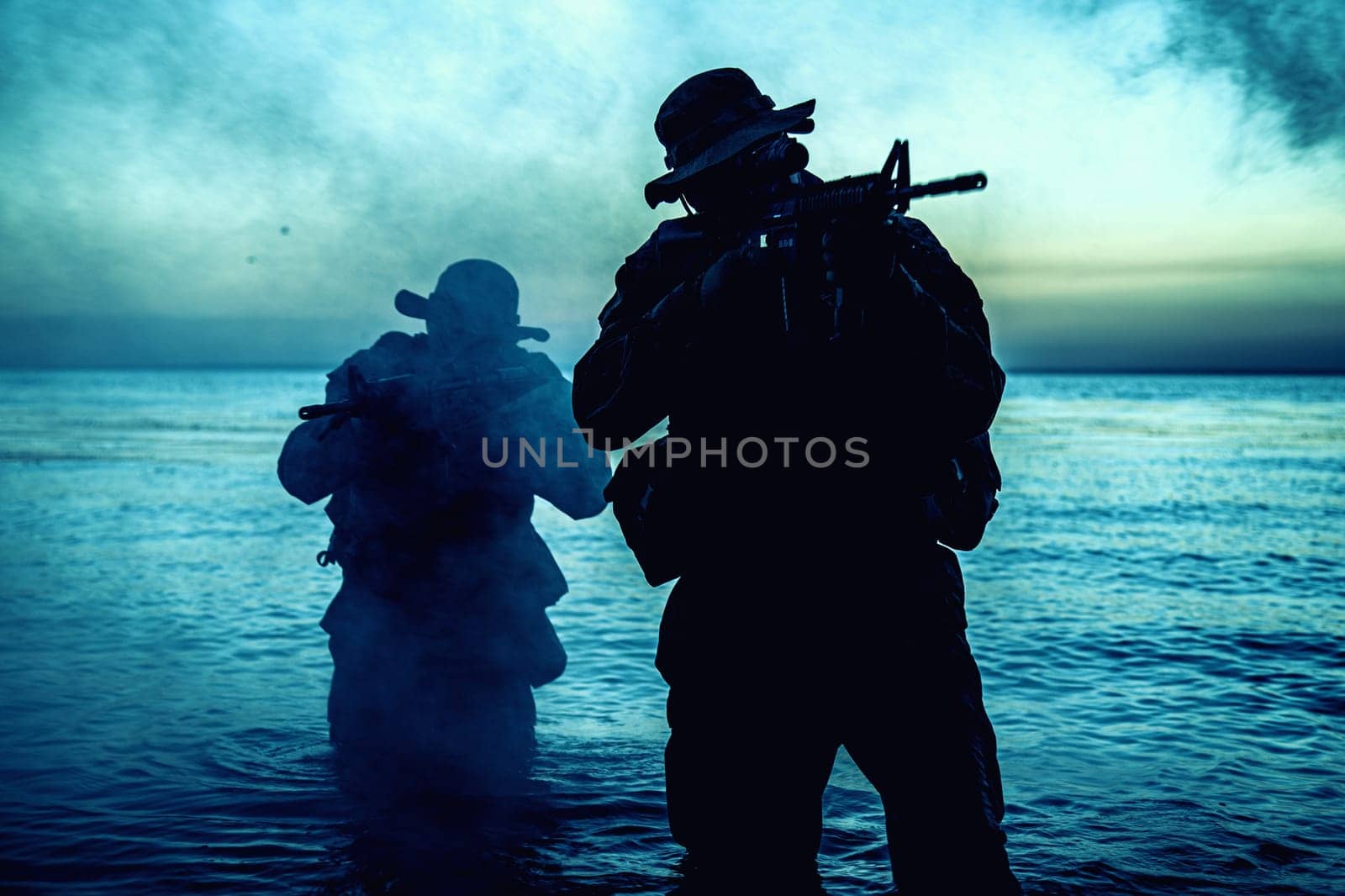 Commando soldiers walking in water, army special operations forces fighters sneaking in darkness, aiming assault rifles and observing shore during amphibious operation on coast at night or dawn