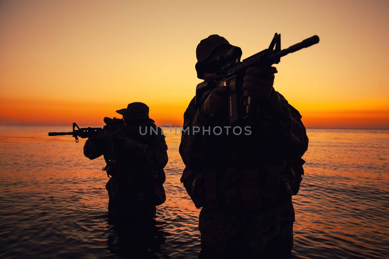Two commando soldiers, army special operations fighters aiming assault rifles while coming out from water on shore at sunset or dawn. Coast guard shooters landing on sea coast, sneaking in water