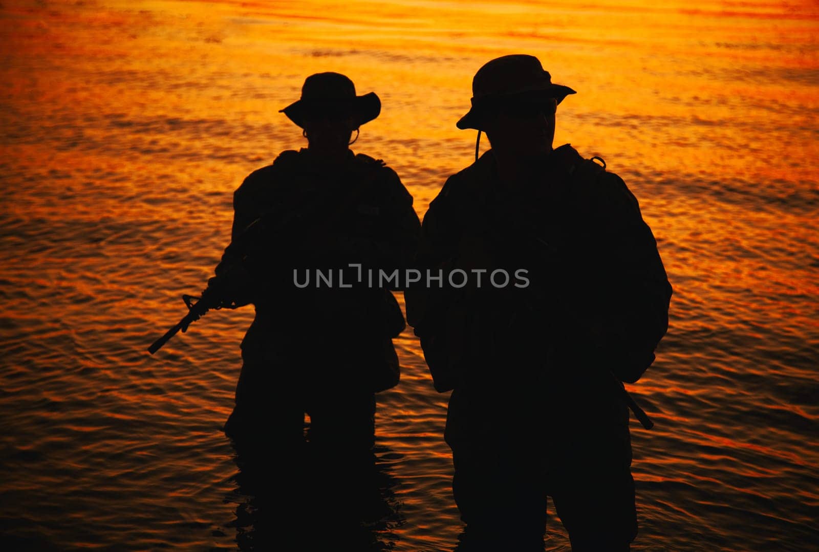 Two commando soldiers, army special operations fighters aiming assault rifles while coming out from water on shore at sunset or dawn. Coast guard shooters landing on sea coast, sneaking in water