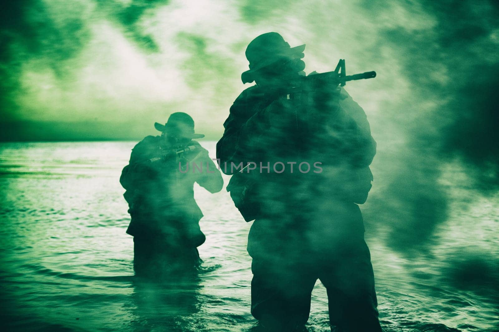 Commando soldiers walking in water, army special operations forces fighters sneaking in darkness, aiming assault rifles and observing shore during amphibious operation on coast at night or dawn
