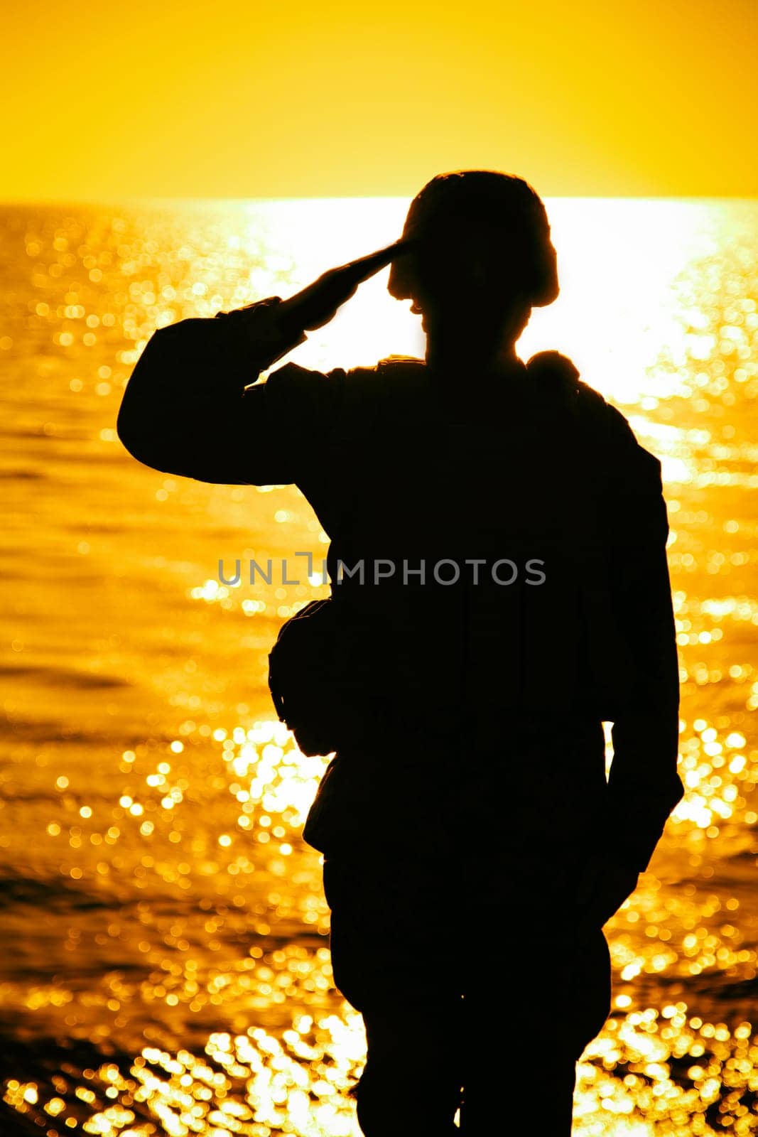 Silhouette of soldier in combat helmet and ammunition saluting on background of sunset sky. Army special forces fighter, Marines rifleman showing respect, greeting officer with salute gesture