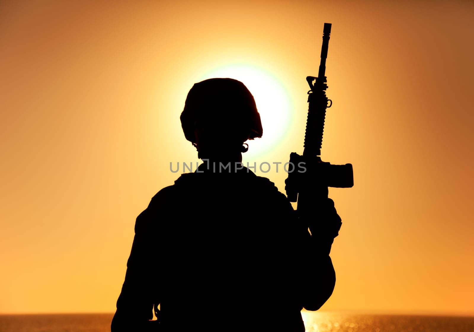 Silhouette of army soldier, special operations forces infantry rifleman, Marines fighter in combat helmet and ammunition standing with assault rifle in hand on background of sunset or dawn sky