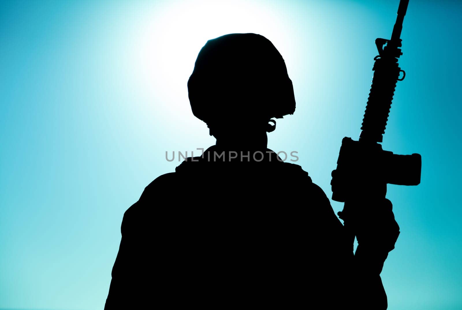 Silhouette of army soldier, special operations forces infantry rifleman, Marines fighter in combat helmet and ammunition standing with assault rifle in hand on background of sunset or dawn sky