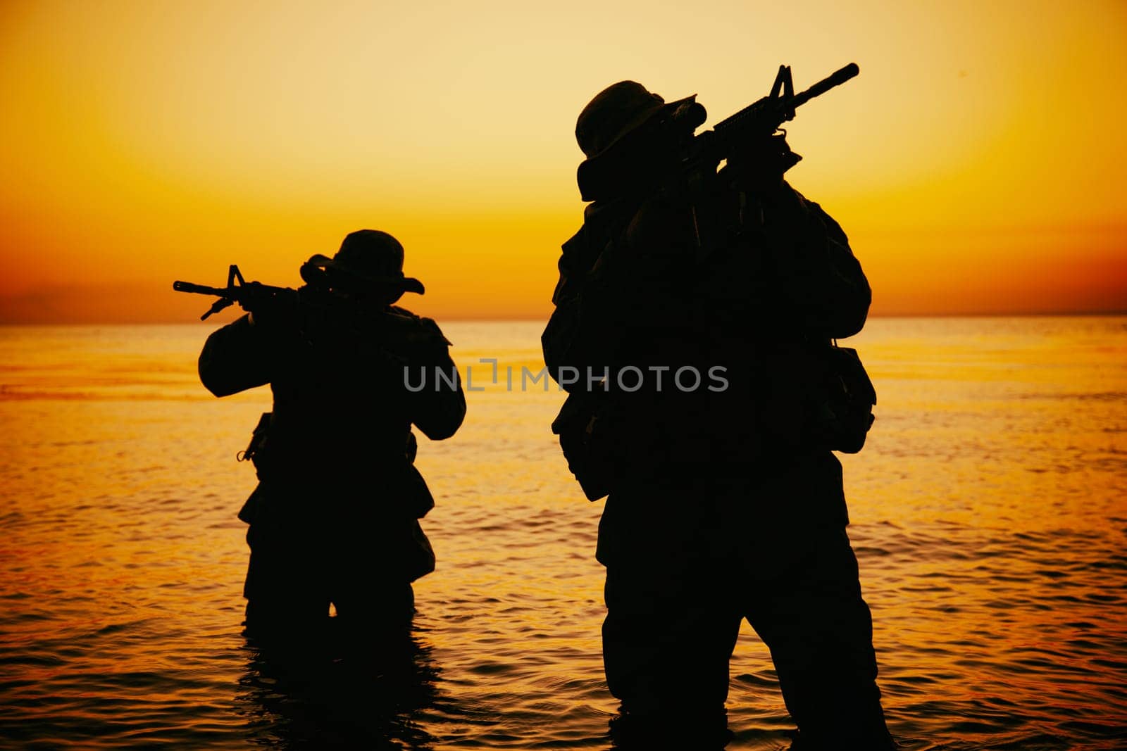 Two commando soldiers, army special operations fighters aiming assault rifles while coming out from water on shore at sunset or dawn. Coast guard shooters landing on sea coast, sneaking in water