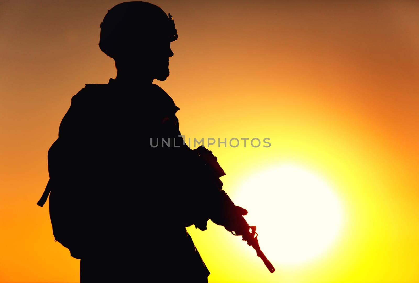 Silhouette of army rifleman in helmet and ammunition, carrying tactical backpack, walking with service rifle on background of sunset sky. Counter terrorist forces fighter marching at night mission