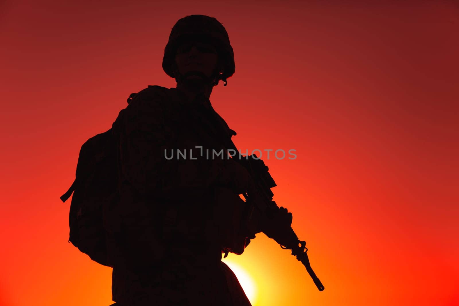 Silhouette of army rifleman in helmet and ammunition, carrying tactical backpack, walking with service rifle on background of sunset sky. Counter terrorist forces fighter marching at night mission