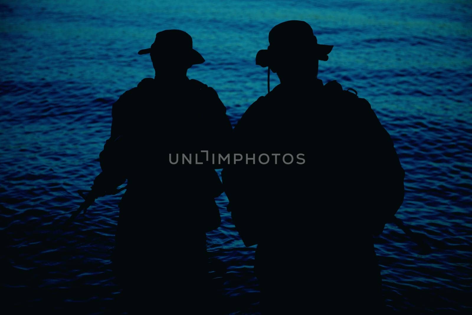 Two commando soldiers, army special operations fighters aiming assault rifles while coming out from water on shore at sunset or dawn. Coast guard shooters landing on sea coast, sneaking in water
