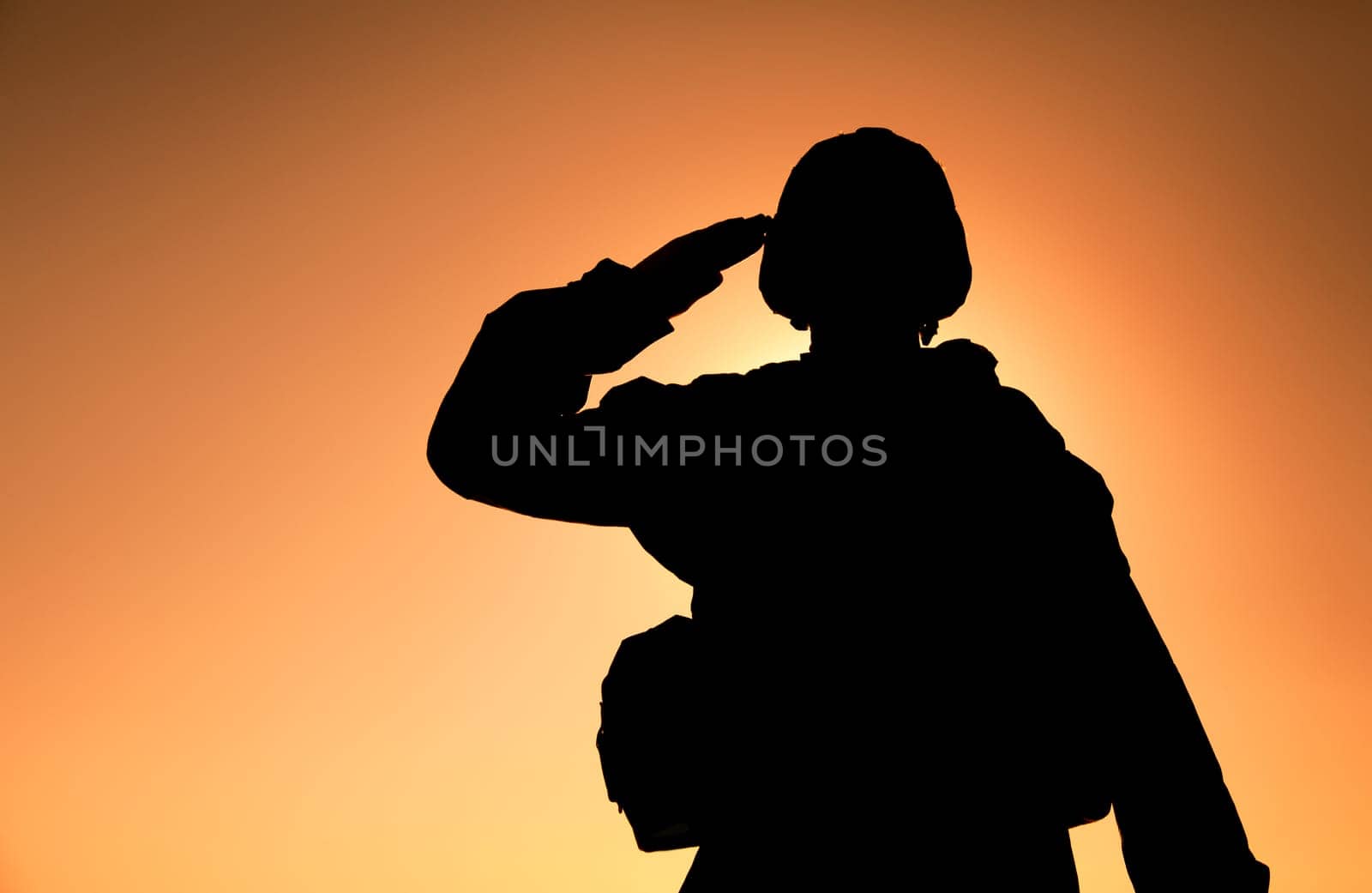 Silhouette of soldier in combat helmet and ammunition saluting on background of sunset sky. Army special forces fighter, Marines rifleman showing respect, greeting officer with salute gesture