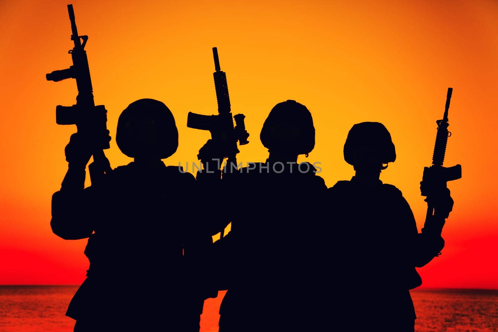Silhouette of army special operations forces soldiers team, group of Marines or coast guard fighters crew in ammunition and combat helmets standing on seashore at sunset with raised assault rifles