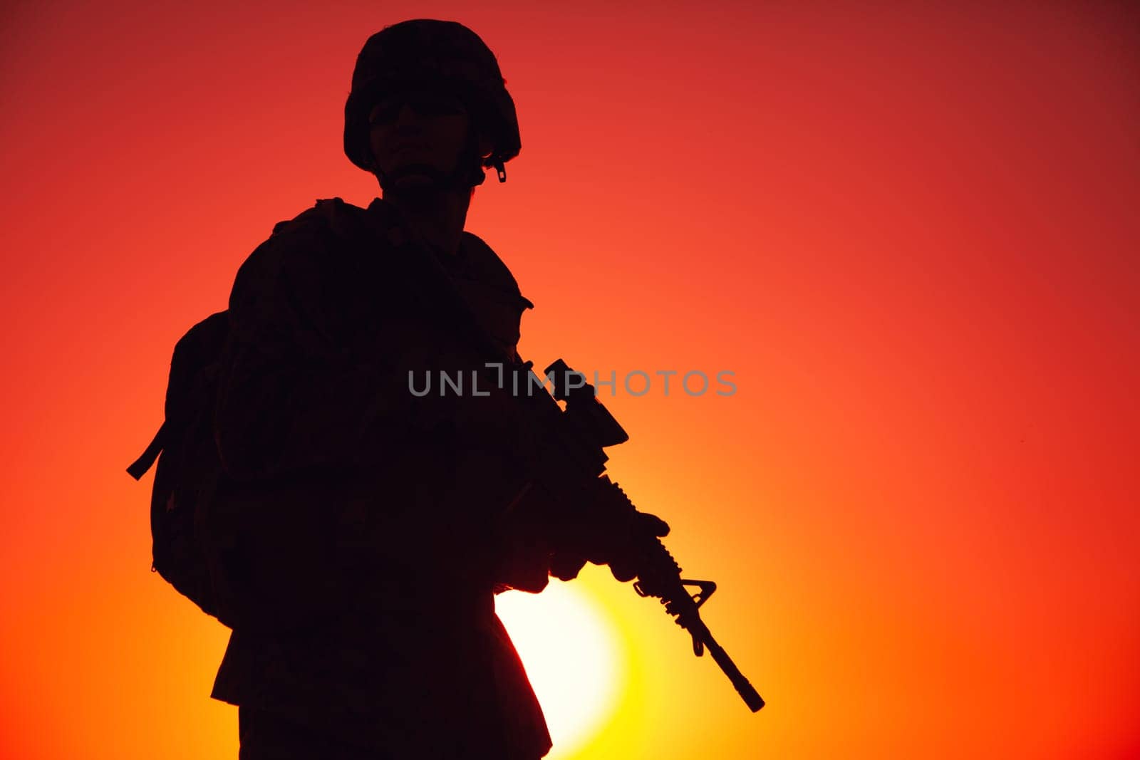 Silhouette of army special forces rifleman, Marines, coast guard or anti-terrorist squad soldier in ammunition and helmet, armed service rifle, standing on ocean shore, patrolling seacoast at sunset