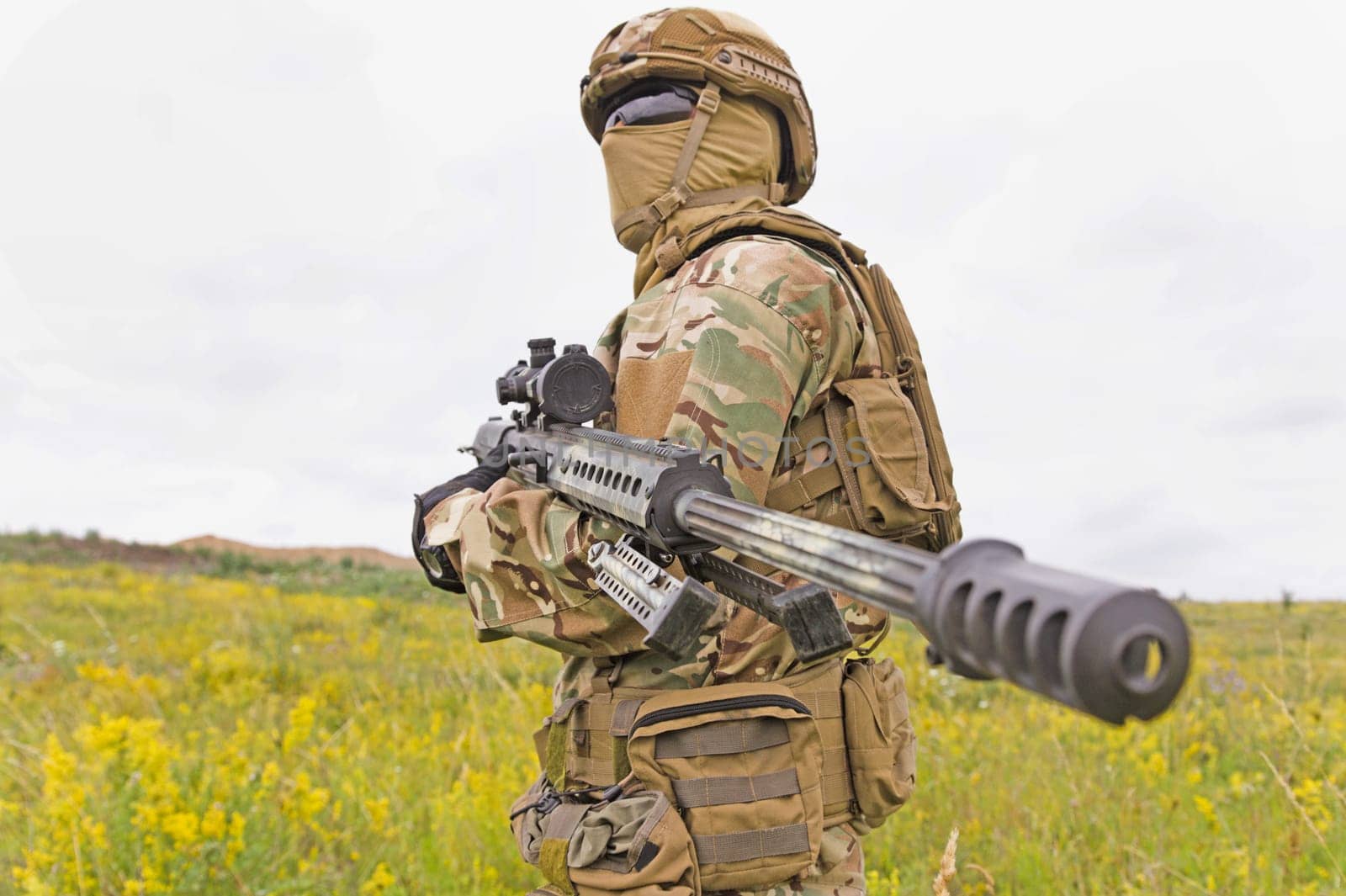 Special forces soldier standing in the green field with sniper rifle
