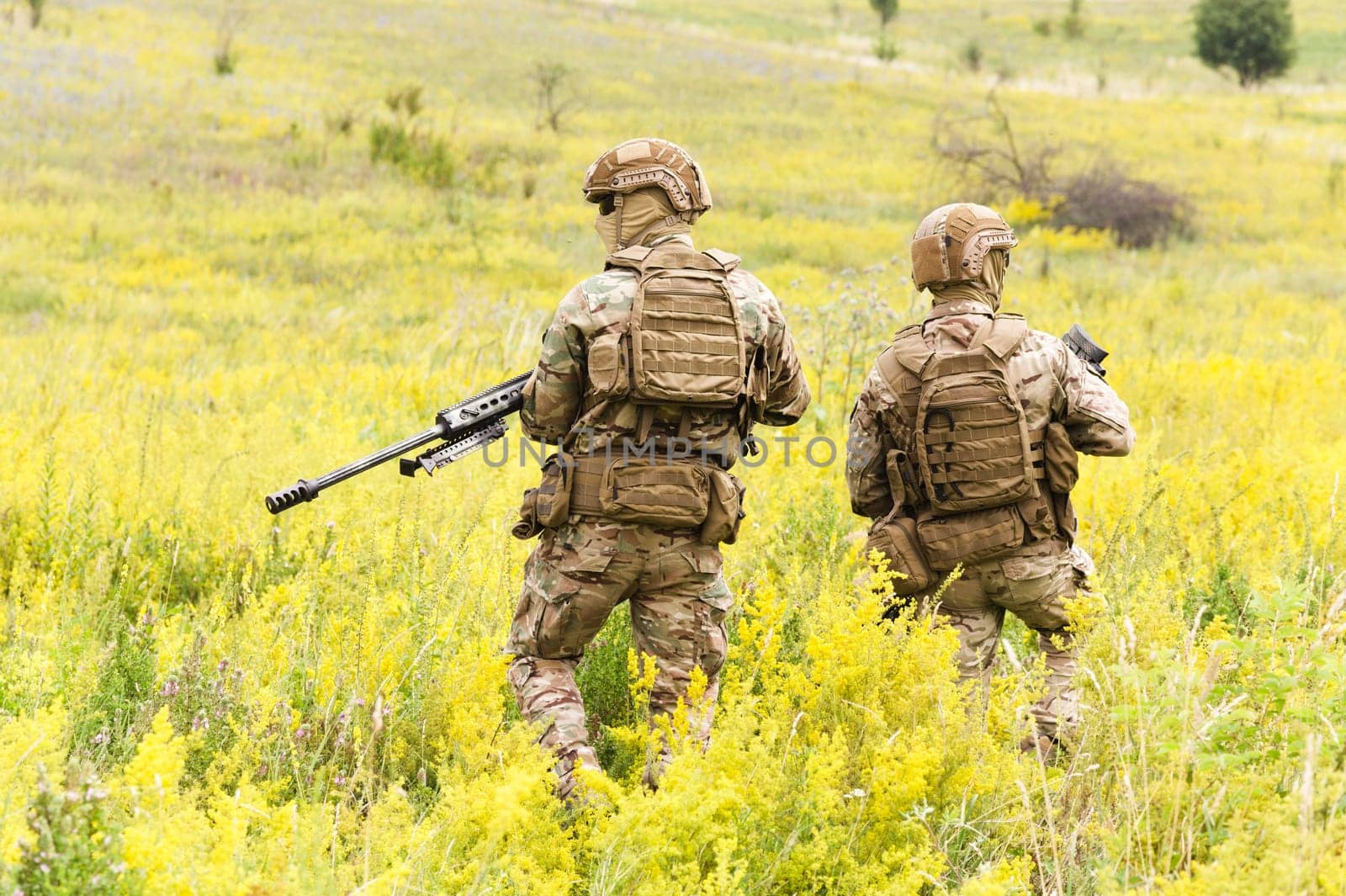 Two equipped and armed special forces soldiers with rifles in the blooming field