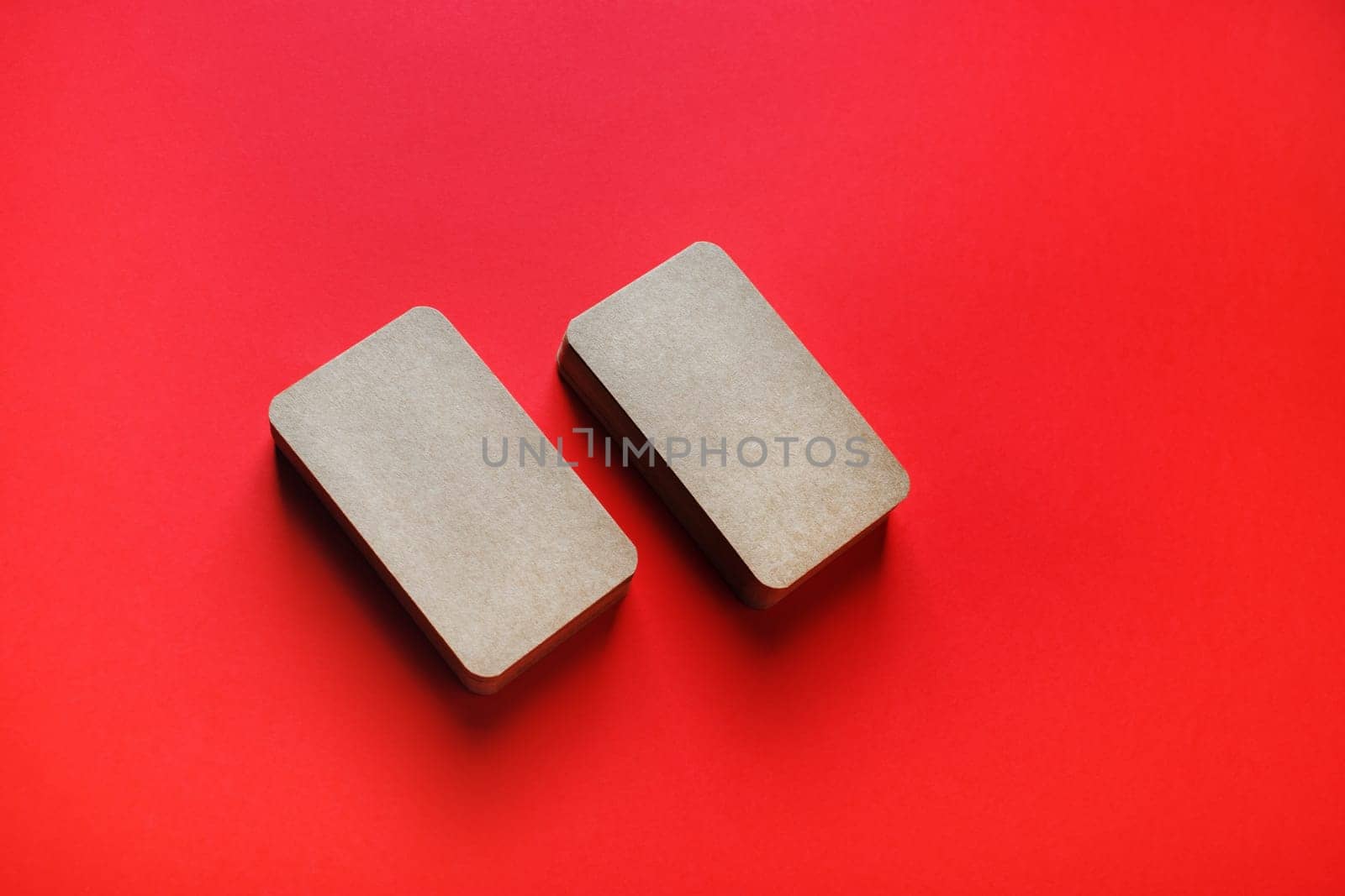 Photo of blank kraft business cards on red paper background. Template for branding identity.
