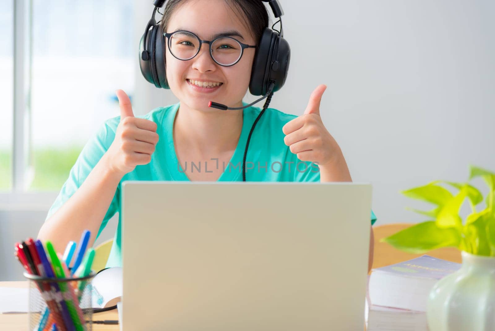 Portrait Asian young woman student glasses headphones happy study smile looking two thumbs up online class college learning internet education teenage girl work distance on a laptop computer from home