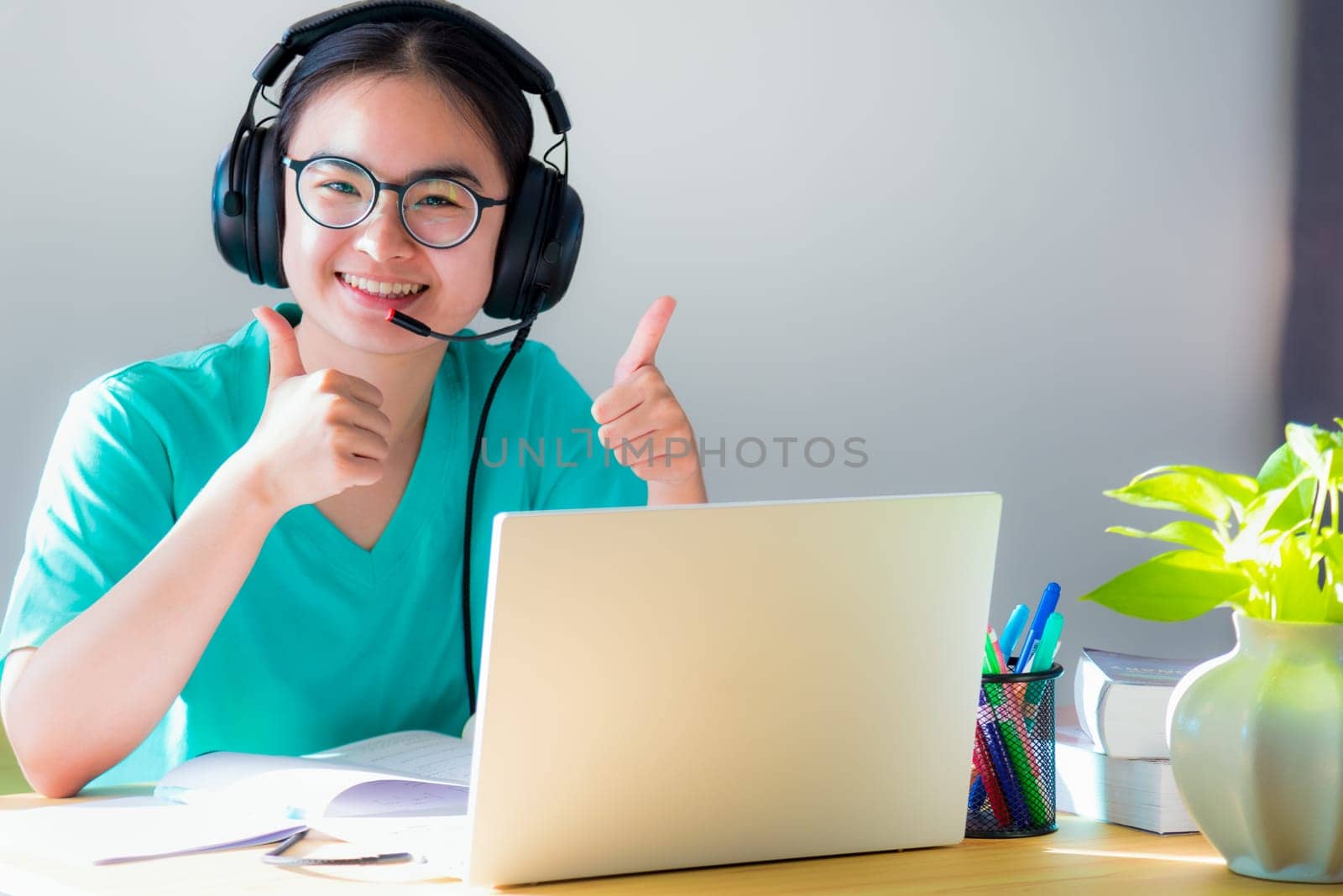 Portrait Asian young woman student glasses headphones happy study smile looking two thumbs up online class college learning internet education teenage girl work distance on a laptop computer from home