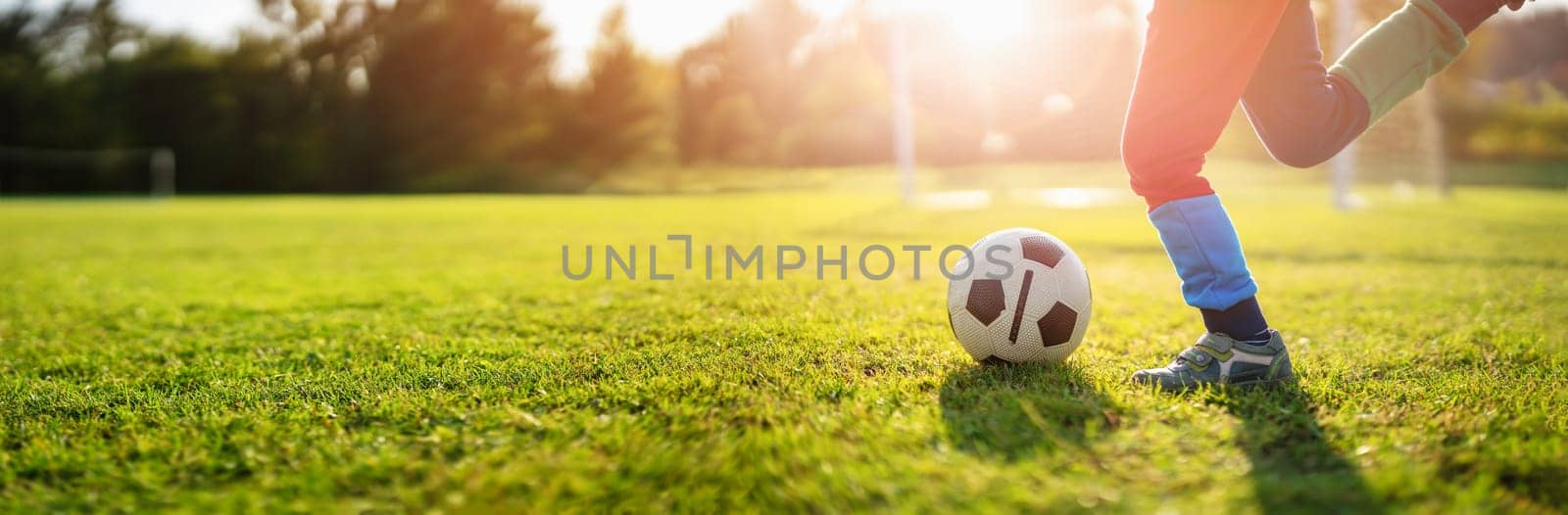 Child playing football on the field with gates. Active boy in summer with ball