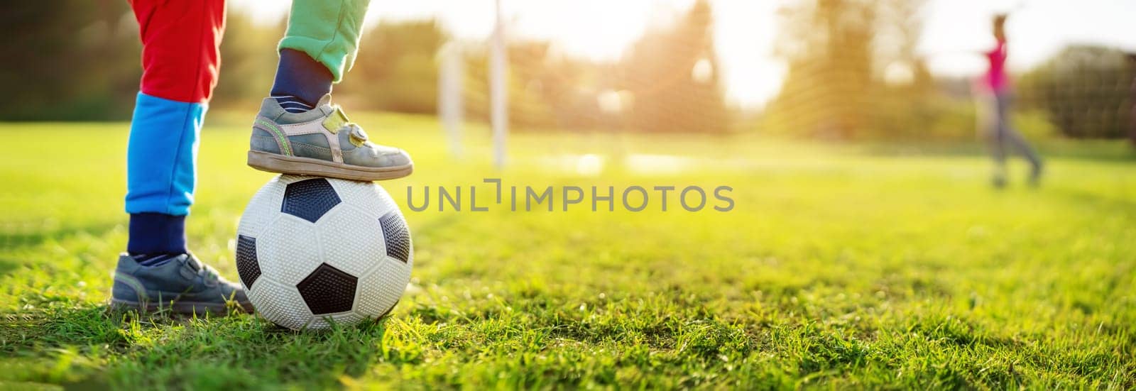 Children playing football on the field with gates. Active boy and girl in summer with ball