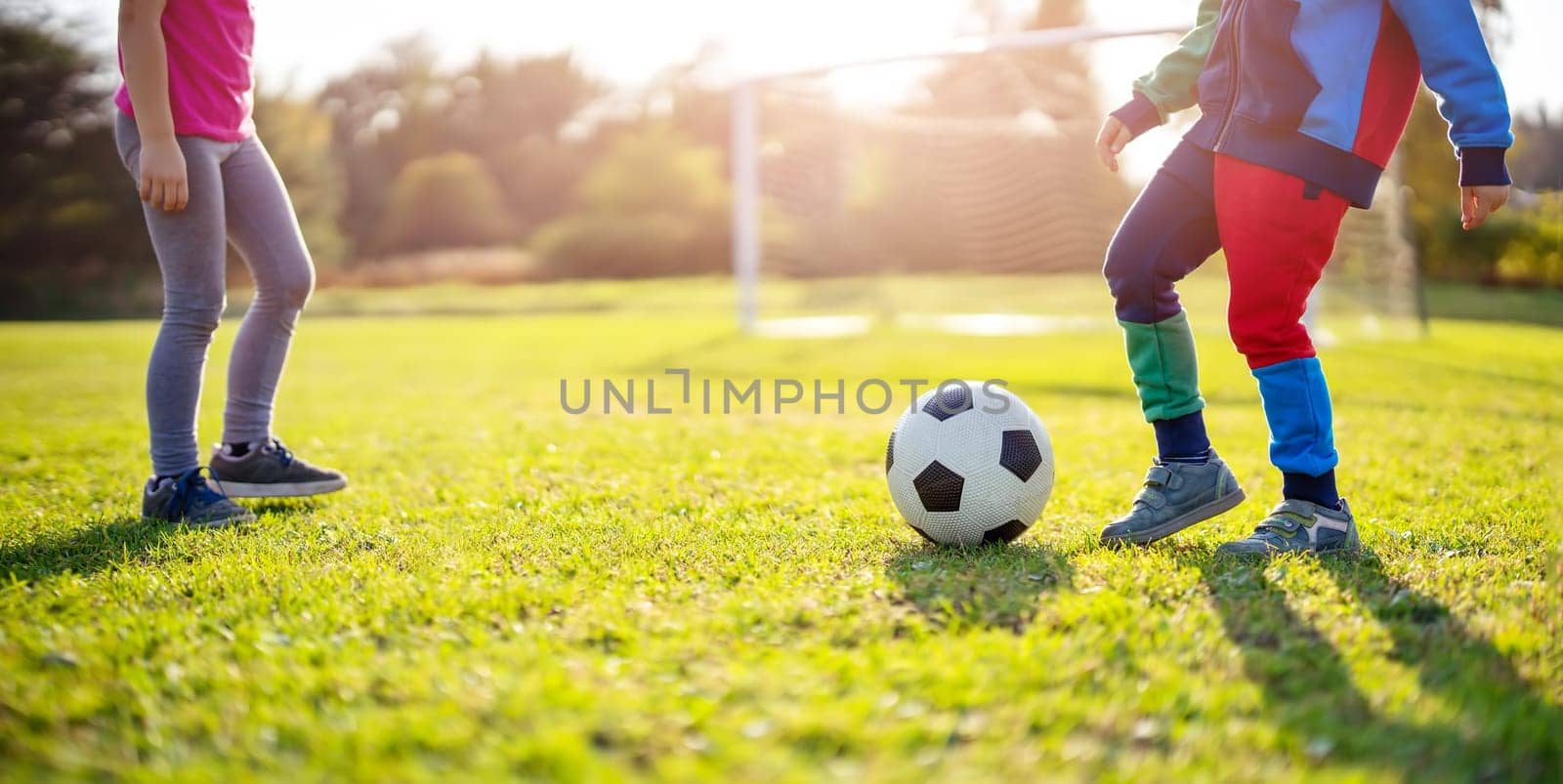 Children playing football on the field with gates. Active boy and girl in summer with ball