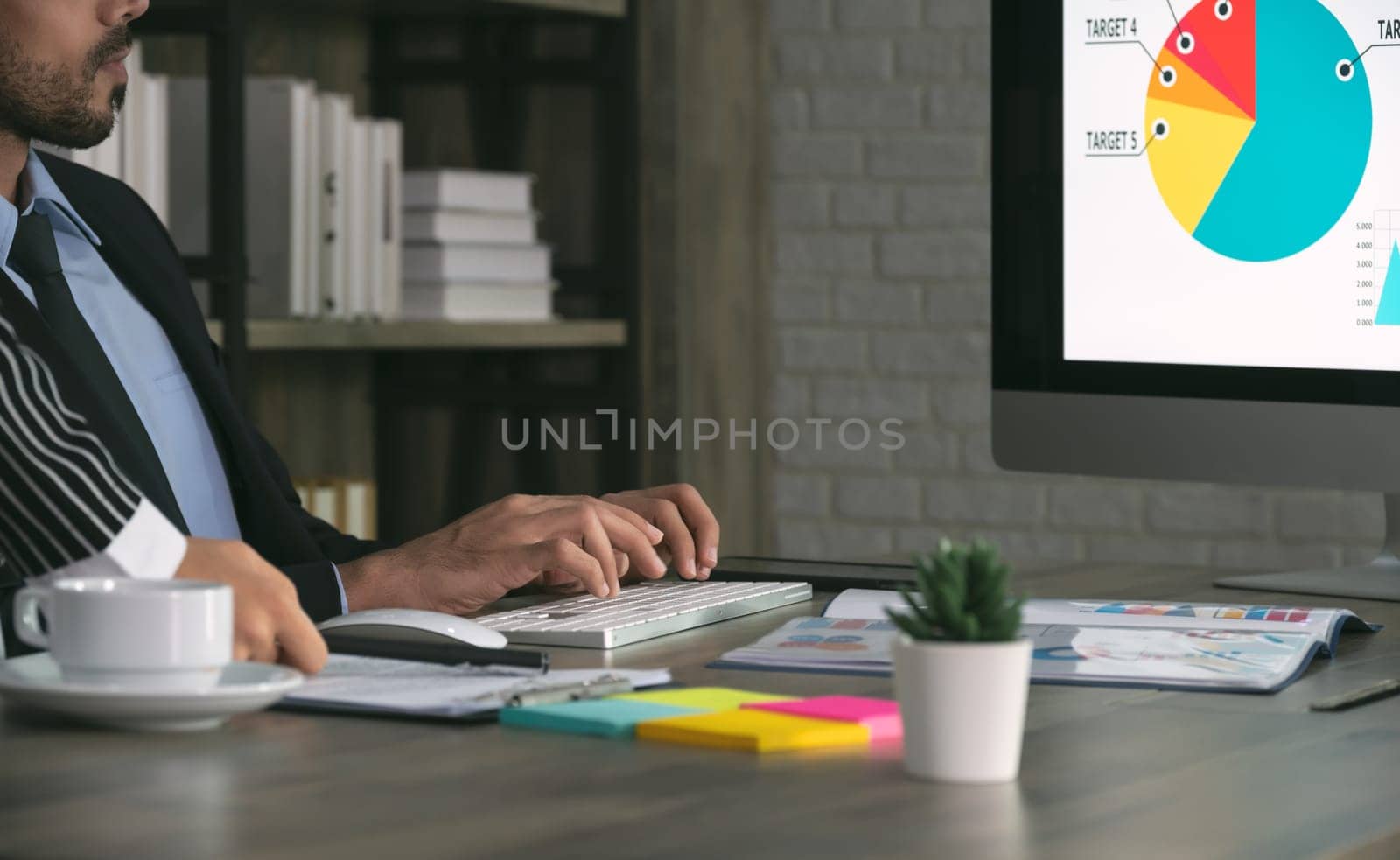 Two business people working together in office. Businessman sitting in office desk and using desktop computer while business woman standing next to him.
