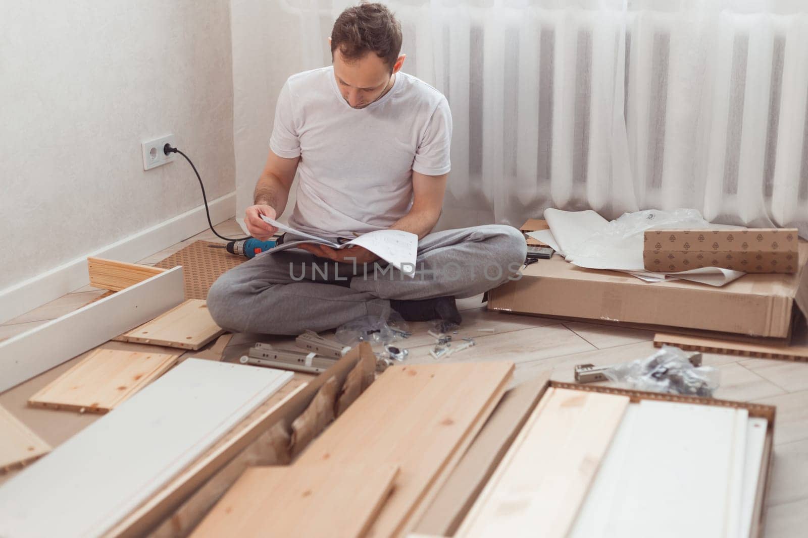 Bewildered man assembling wooden furniture. Difficulties and disadvantages of self-assembly of furniture at home without master. Man reading instructions and misunderstand what to do the next.