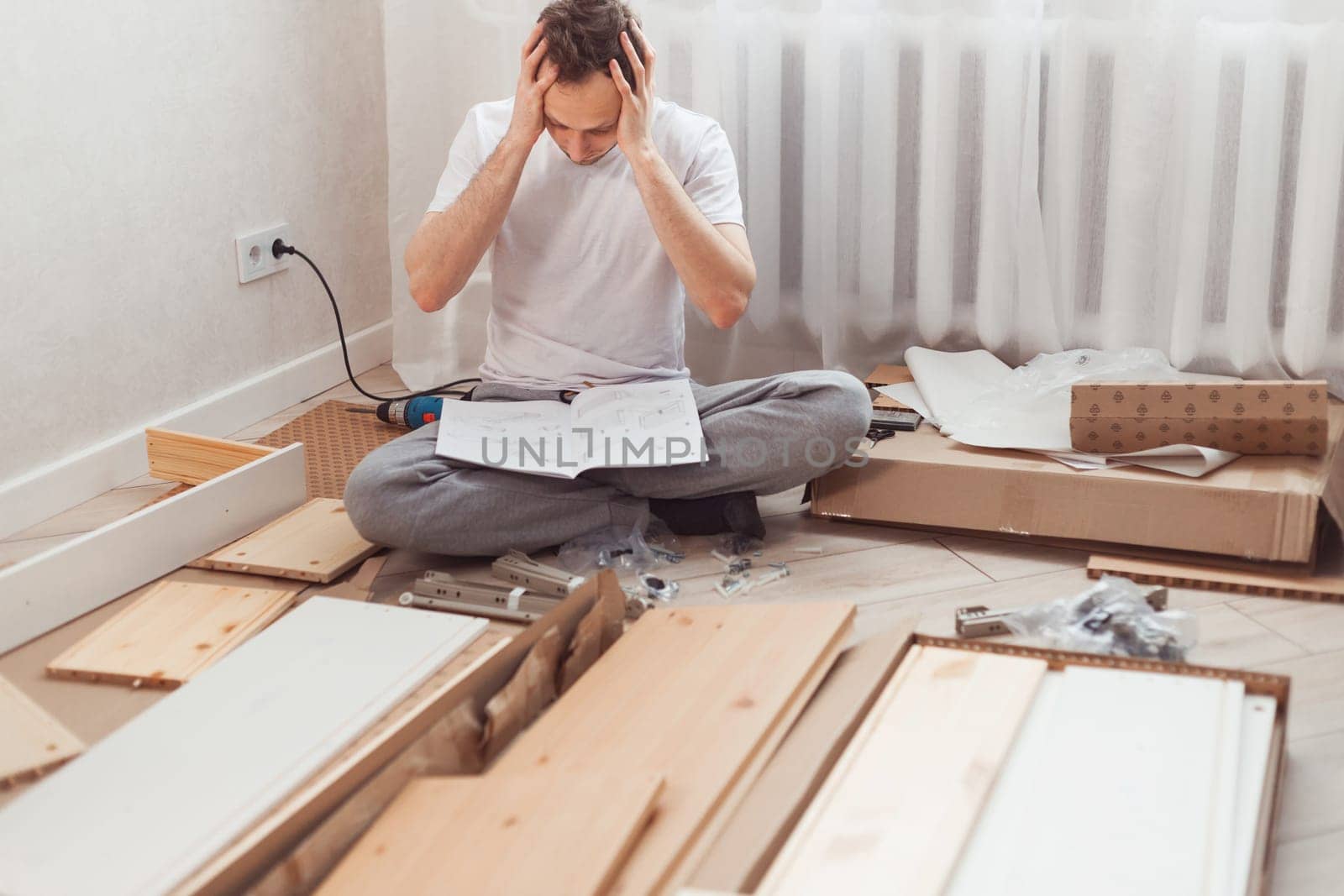 Bewildered man assembling wooden furniture. Difficulties and disadvantages of self-assembly of furniture at home without a master. Man reading instructions and misunderstand what to do the next.
