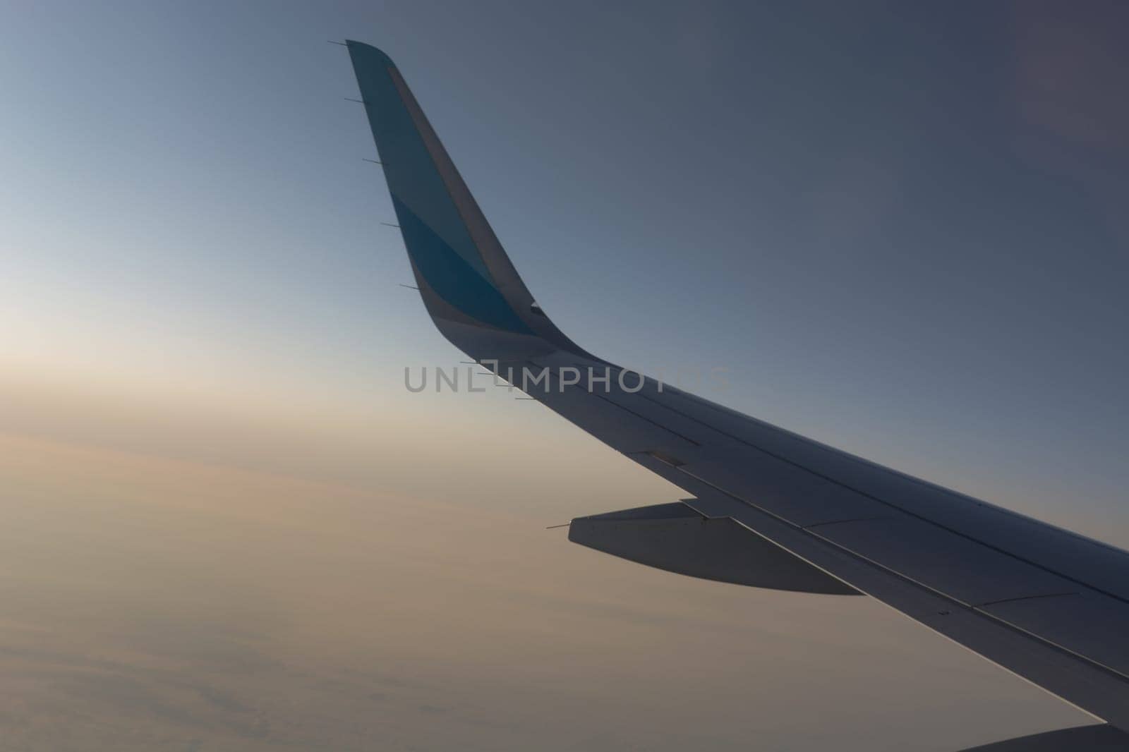 In the air, view of the airplane wing with horizon of dark blue sky and clouds background in sunrise time, viewed from the airplane window