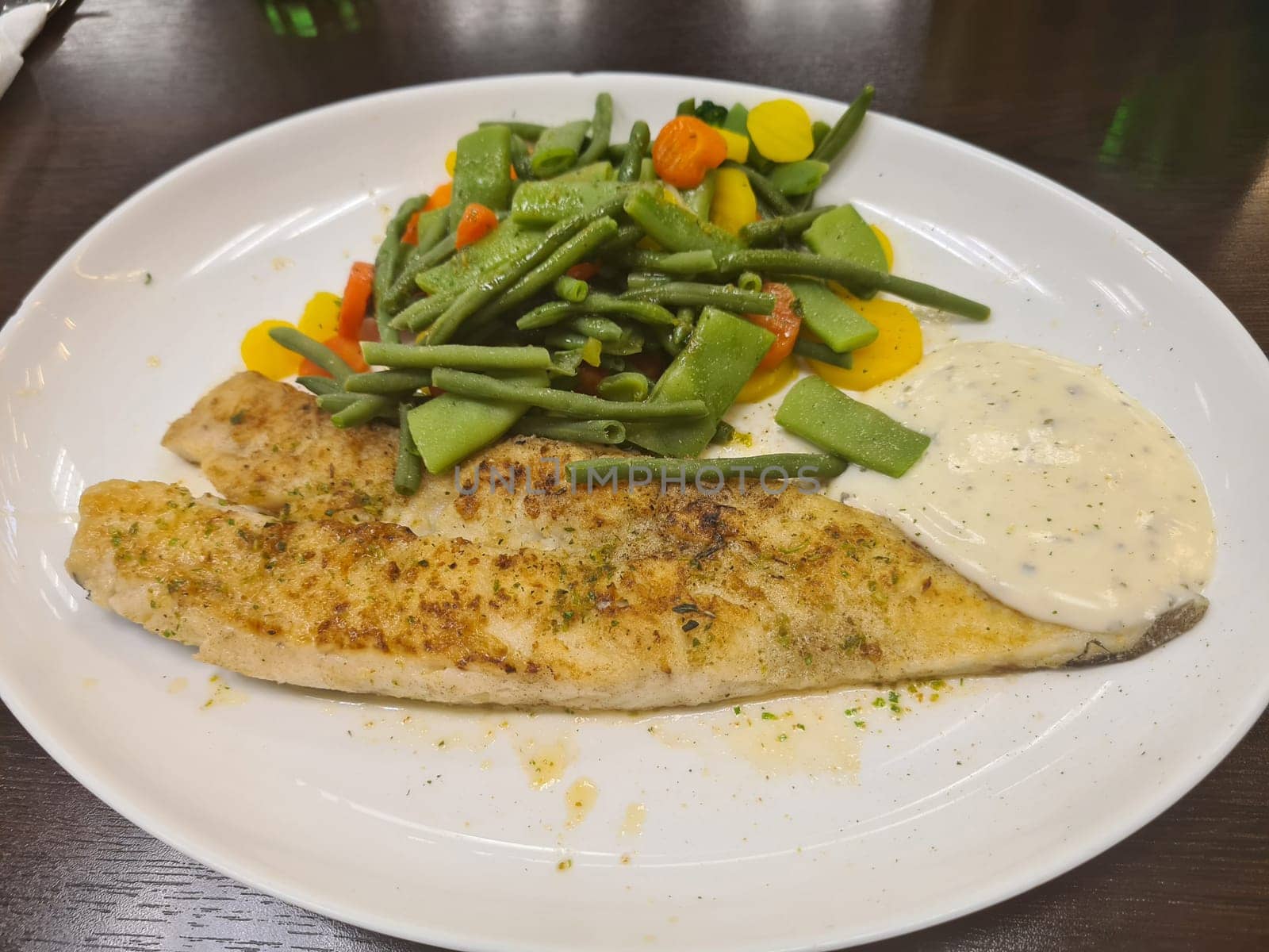 To portions of fresh grilled pollock or coalfish served with colorful salad and slices of lemon, close up high angle view